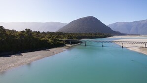 Une rivière traversée par un pont, entourée de montagnes et d’une forêt dense.