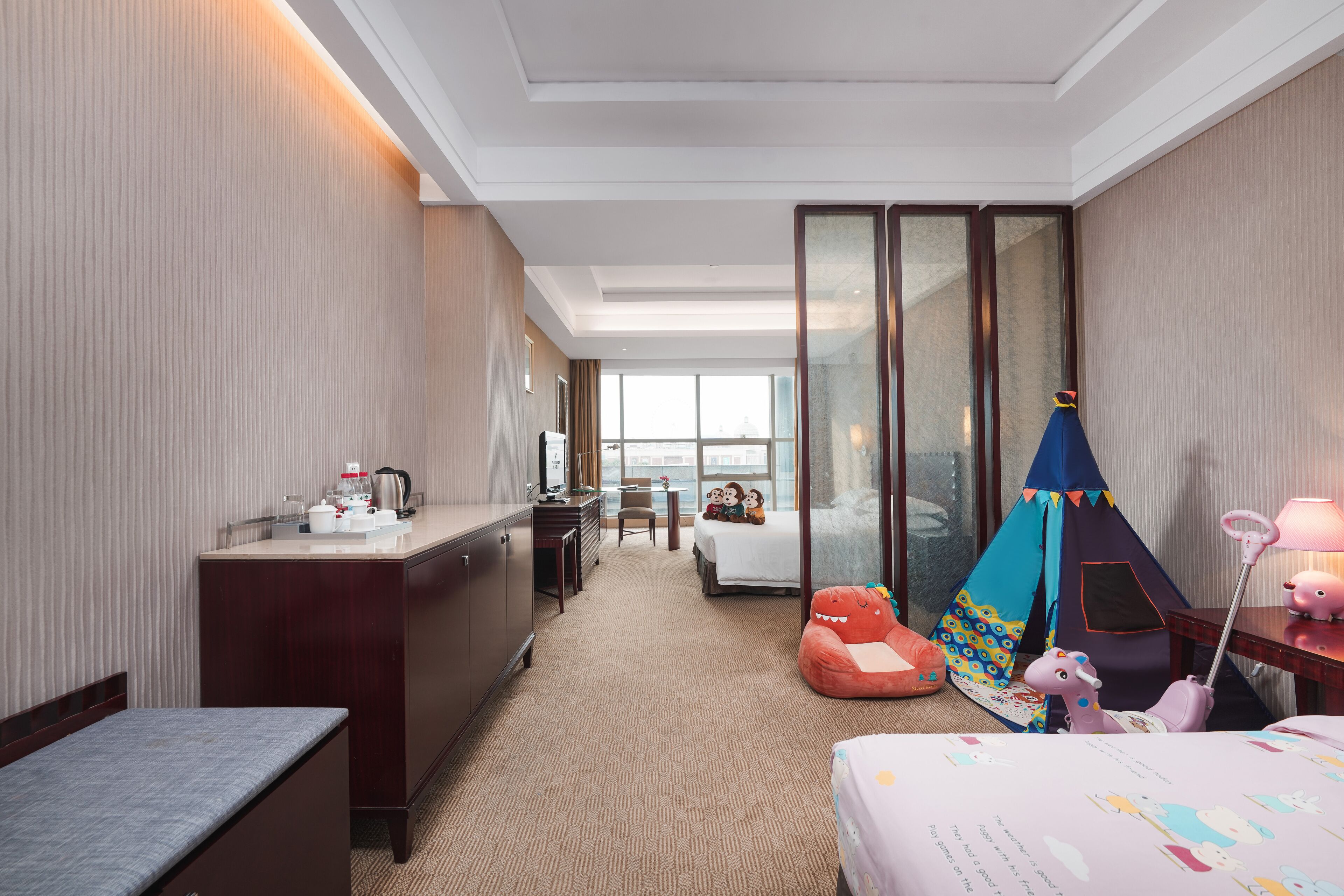 A hotel room with a bed, a desk, a chair, a kitchenette, a tent, and a view of the city.