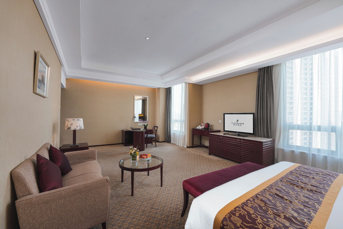 Habitación de hotel con cama, sofá, escritorio, televisión y vistas a la ciudad.