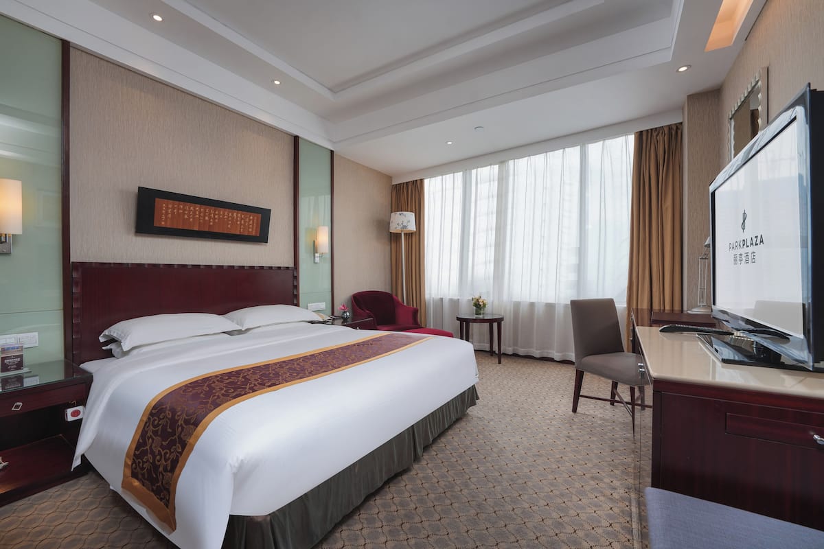 A hotel room with a large bed, a desk, a TV, and a window with curtains.