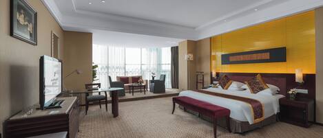 A hotel room with a large bed, a desk, a chair, a small table, and a sofa.