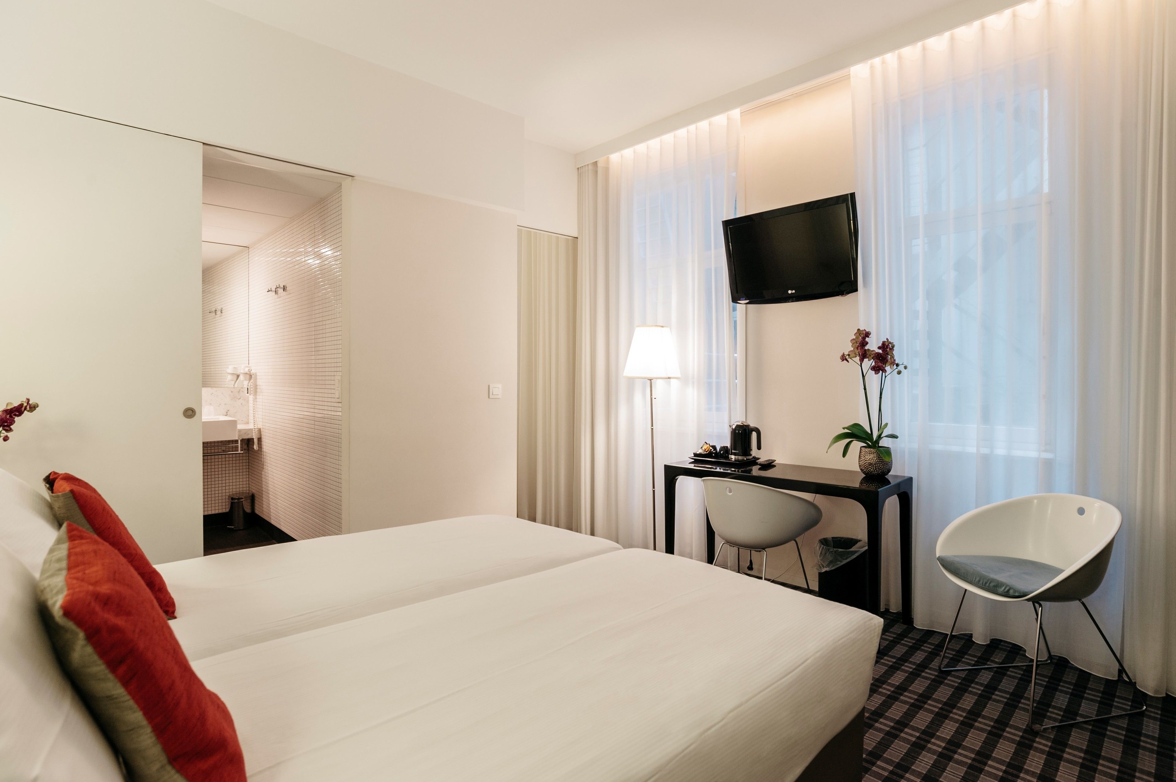 Ein Hotelzimmer mit einem Bett, einem Schreibtisch mit Stuhl, einem Fernseher und einem Fenster mit Vorhängen.