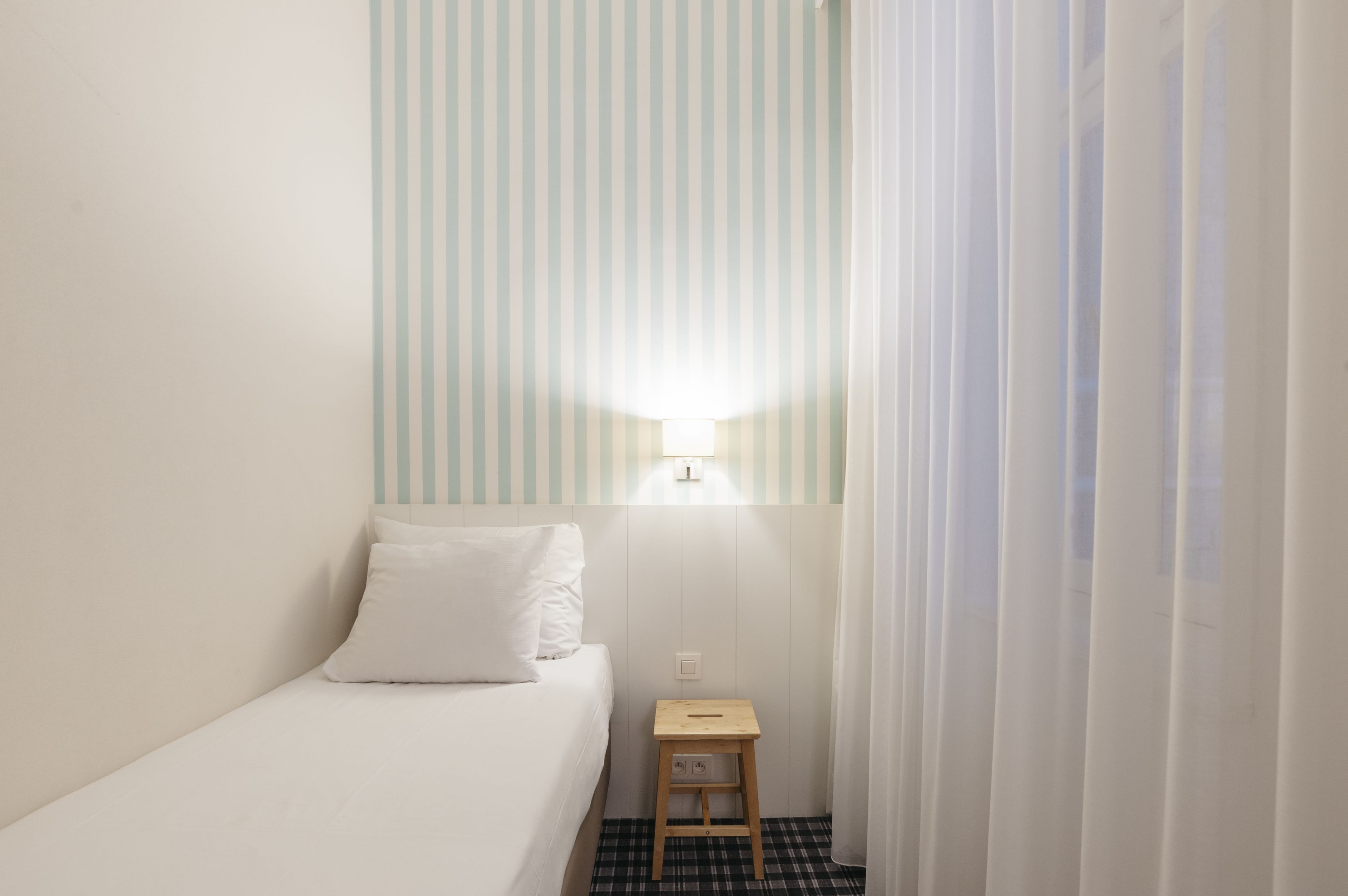 Una stanza piccola e ordinata con un letto singolo, un comodino e una lampada a parete.
