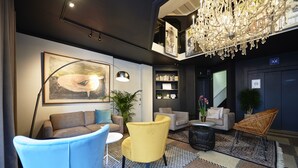 A modern lobby with a chandelier, a large painting, a bookshelf, and a seating area with a blue chair and a yellow armchair. - Leopold Hotel Ostend (Ostend)
