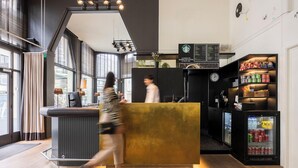 A modern hotel lobby with a reception desk, a clock, and a refrigerator stocked with beverages. - Leopold Hotel Ostend (Ostend)