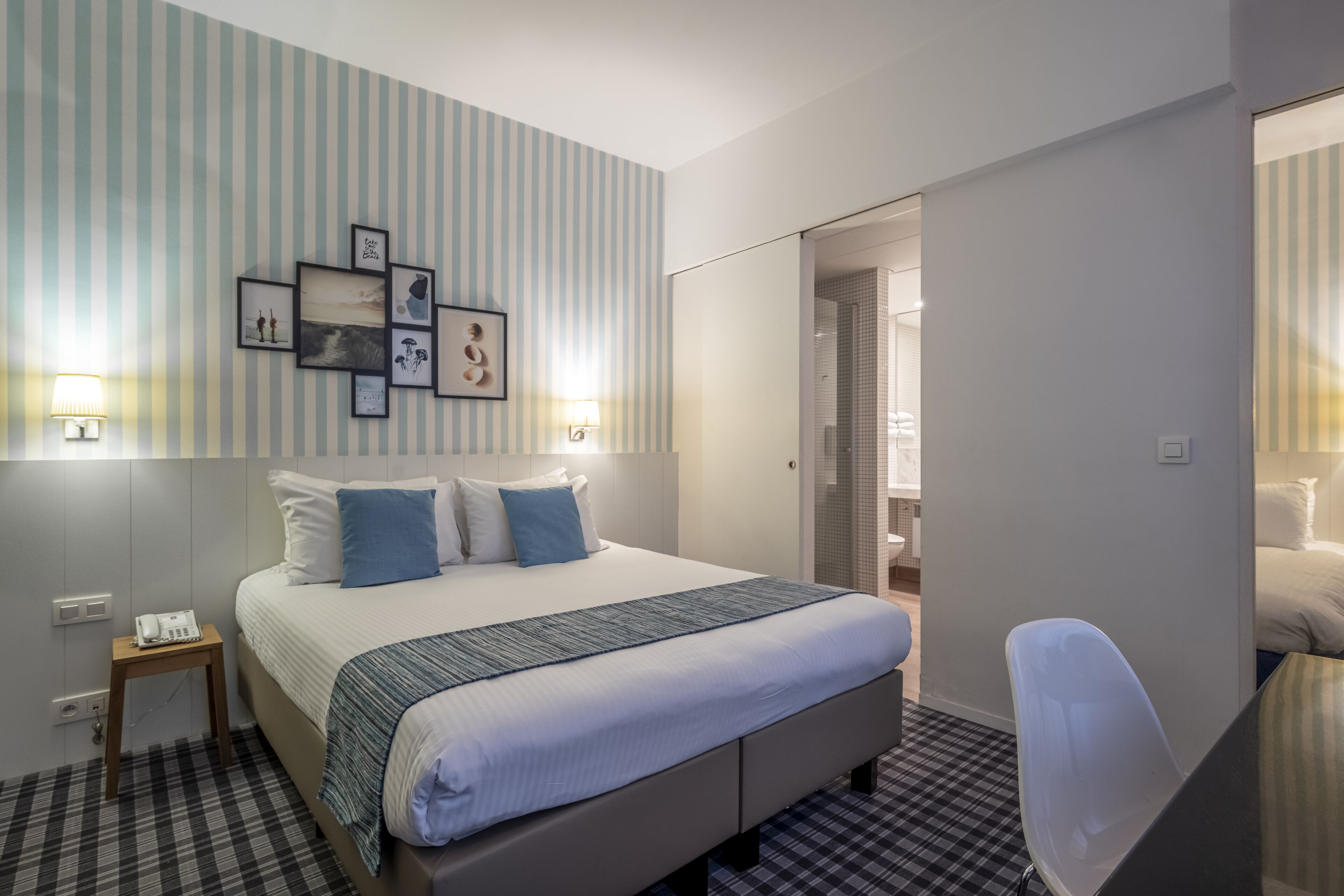 A hotel room with a bed, bedside lamps, a small table, and a chair.