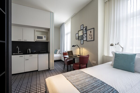 Habitación de hotel con cama, escritorio, silla, computadora portátil, microondas y kitchenette.