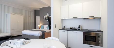 A modern hotel room with a neatly made bed, a dining table set with plates and glasses, and a kitchenette with a microwave and cabinets.