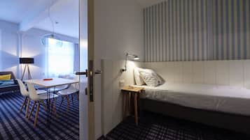 A modern hotel room with a bed, bedside table, lamp, and a dining area with chairs and a table.