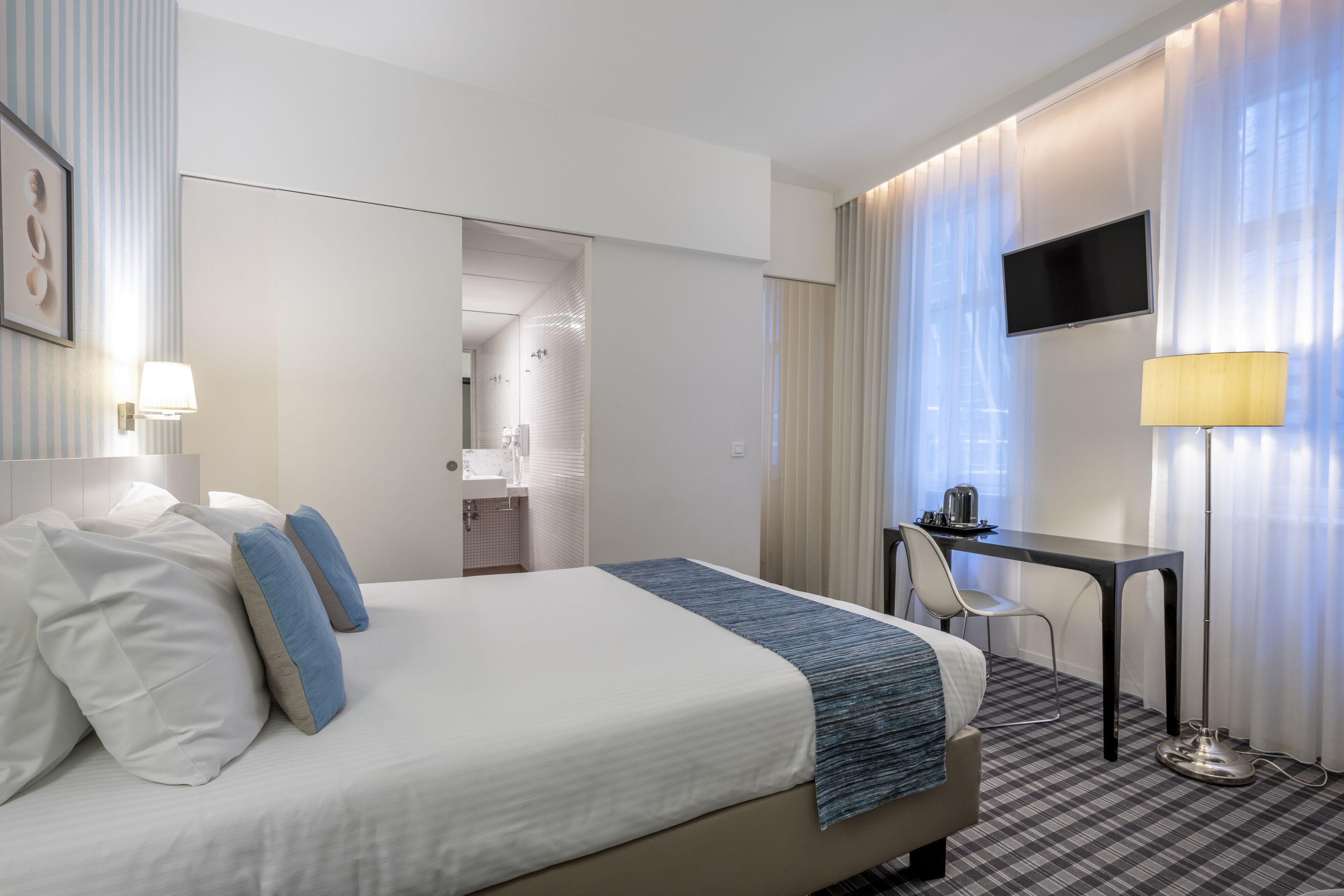 Ein Hotelzimmer mit einem Bett, einem Schreibtisch, einem Sessel, einem Fernseher und einer Lampe.