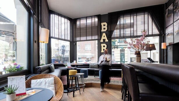 A modern bar area with seating, large windows, and a city view. - Leopold Hotel Ostend (Ostend)