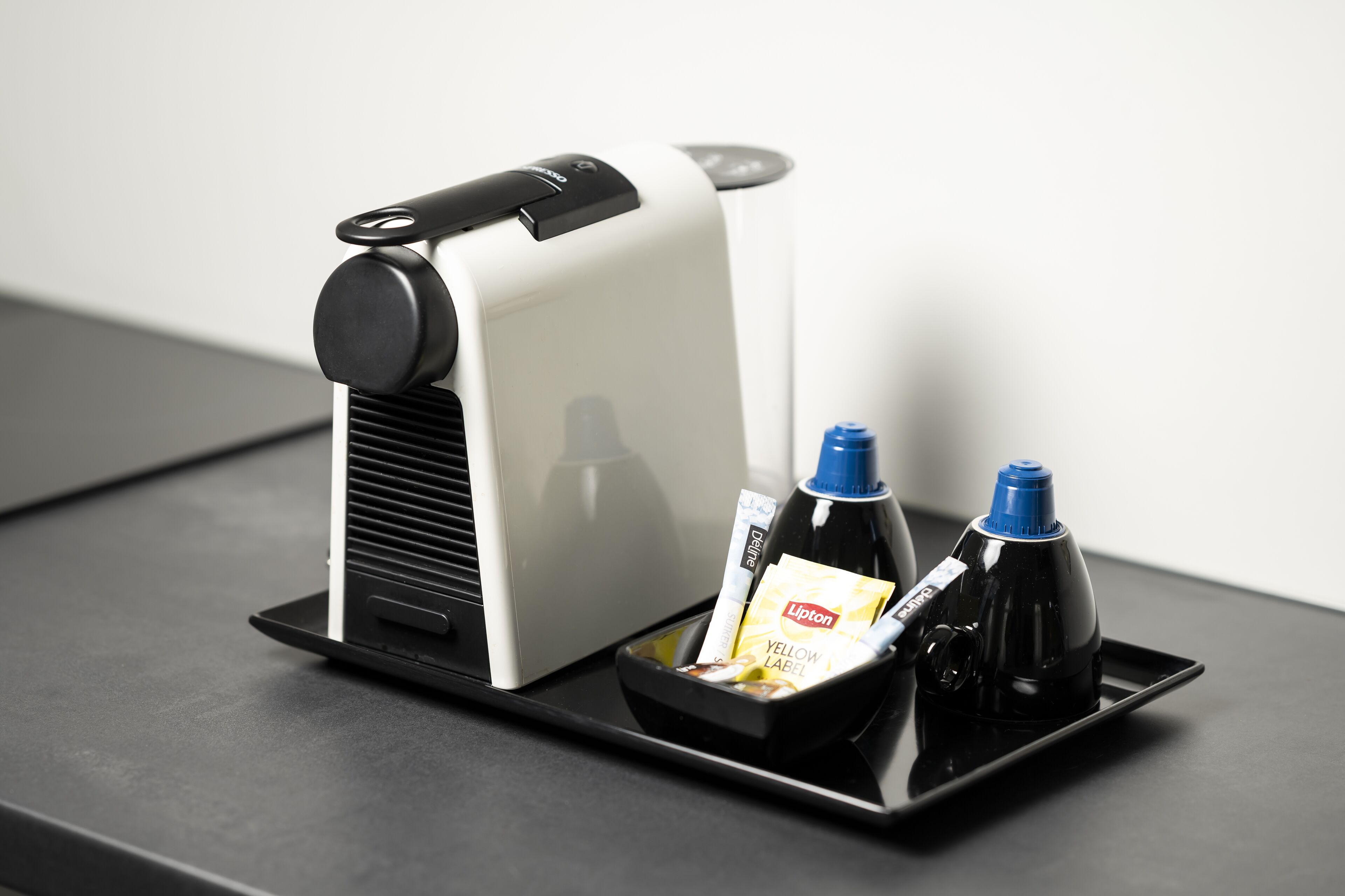 A coffee machine with a tray containing a Lipton tea bag, a yellow label, and two bottles.