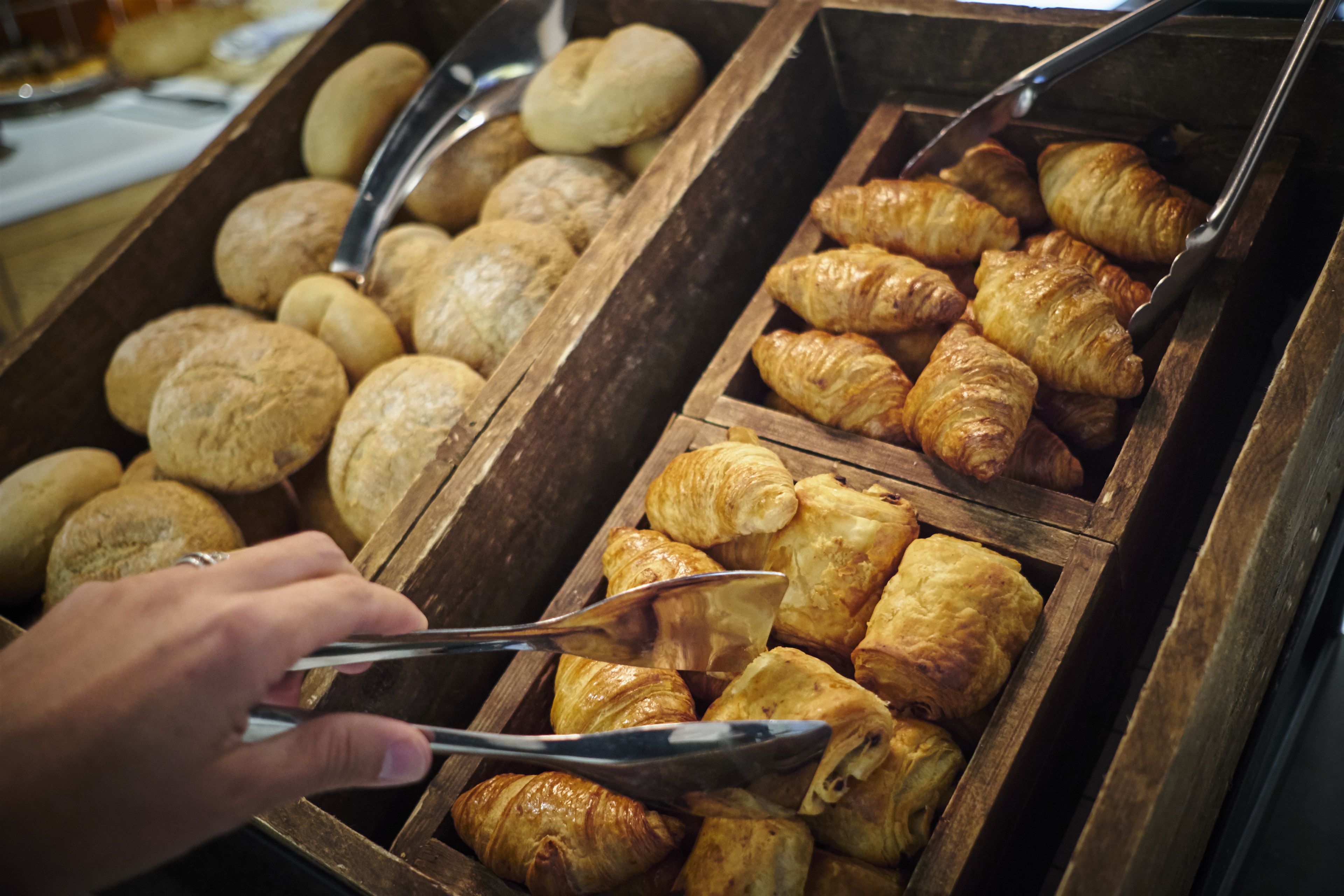 A wooden display case with various baked goods, including croissants and bread.