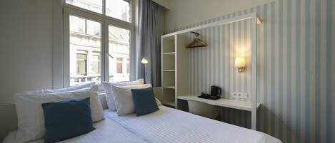 A hotel room with a large bed, a desk, and a wardrobe.