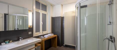 A modern bathroom with a glass-enclosed shower, a vanity with a mirror, and a wooden bench.