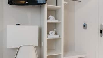 A modern hotel room with a flat-screen TV mounted on the wall, a white chair, a built-in shelving unit, and a door with a keycard reader.