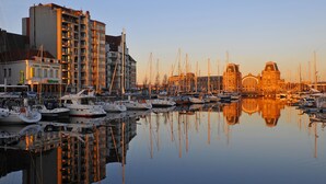 A marina with boats docked, a building with a large arched window, and a reflection in the calm water. - Leopold Hotel Ostend (Ostend)