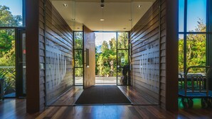 A modern building entrance with wooden paneling, a glass door, and a view of a lush garden. - Legacy Te Waonui Hotel Franz Josef (Franz Josef Glacier)