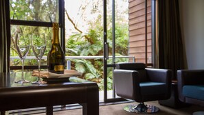 A table with a bottle of champagne and two glasses, a chair, and a view of greenery through a window. - Legacy Te Waonui Hotel Franz Josef (Franz Josef Glacier)