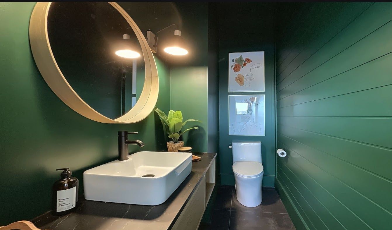 A bathroom with a white sink, a mirror, a toilet, and green walls.