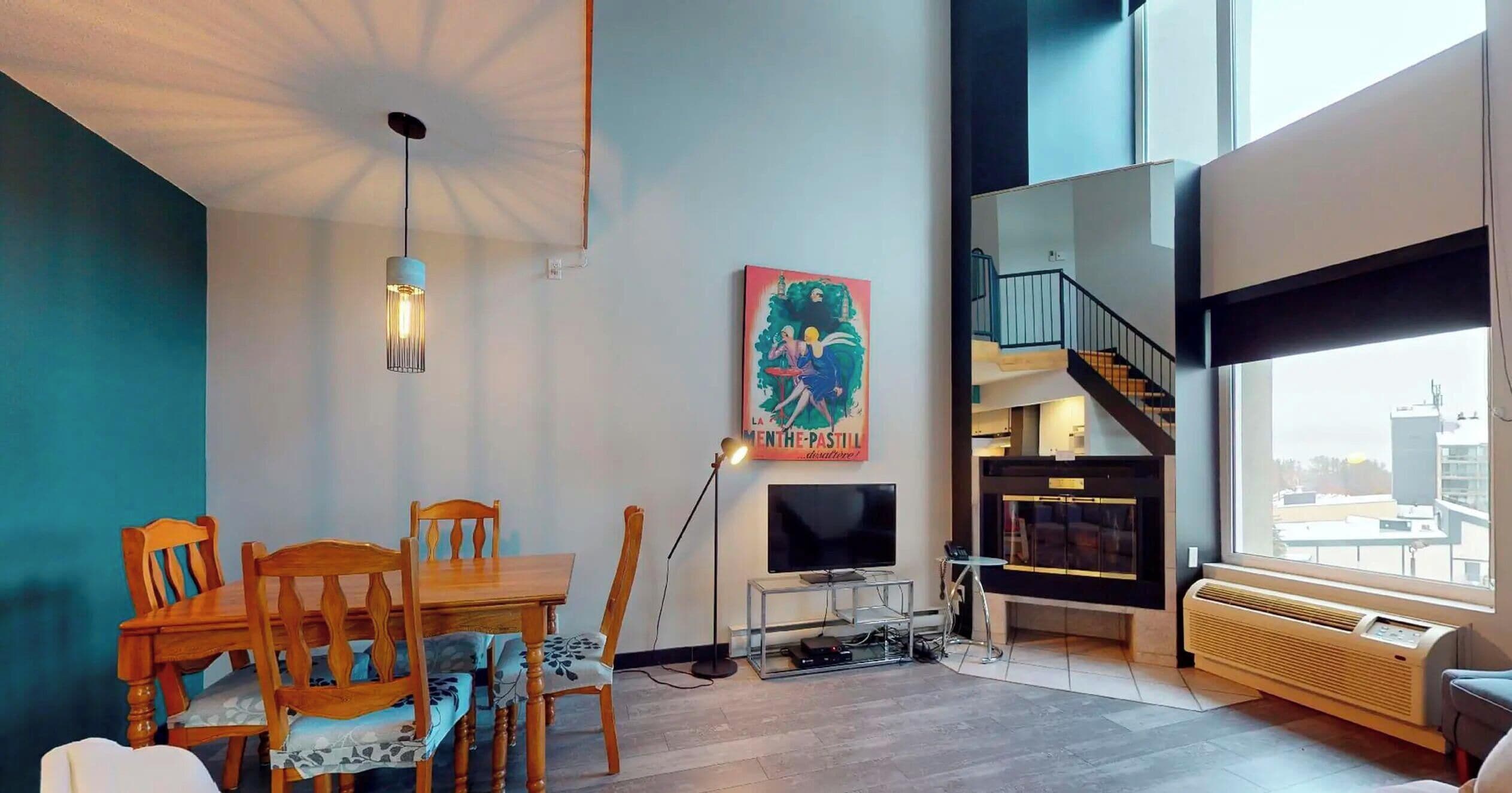 A modern living room with a dining area, a large window, and a staircase leading to an upper level.