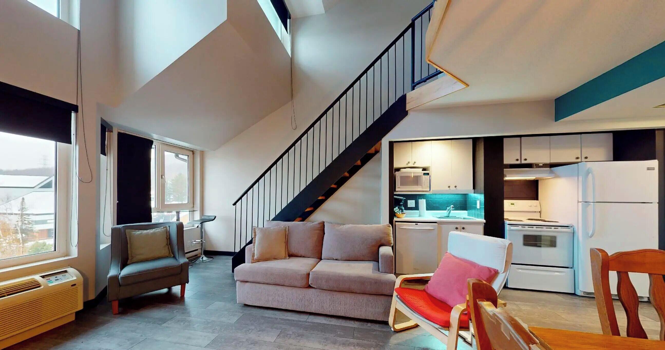 A modern living space with a staircase, a kitchenette, and seating areas.