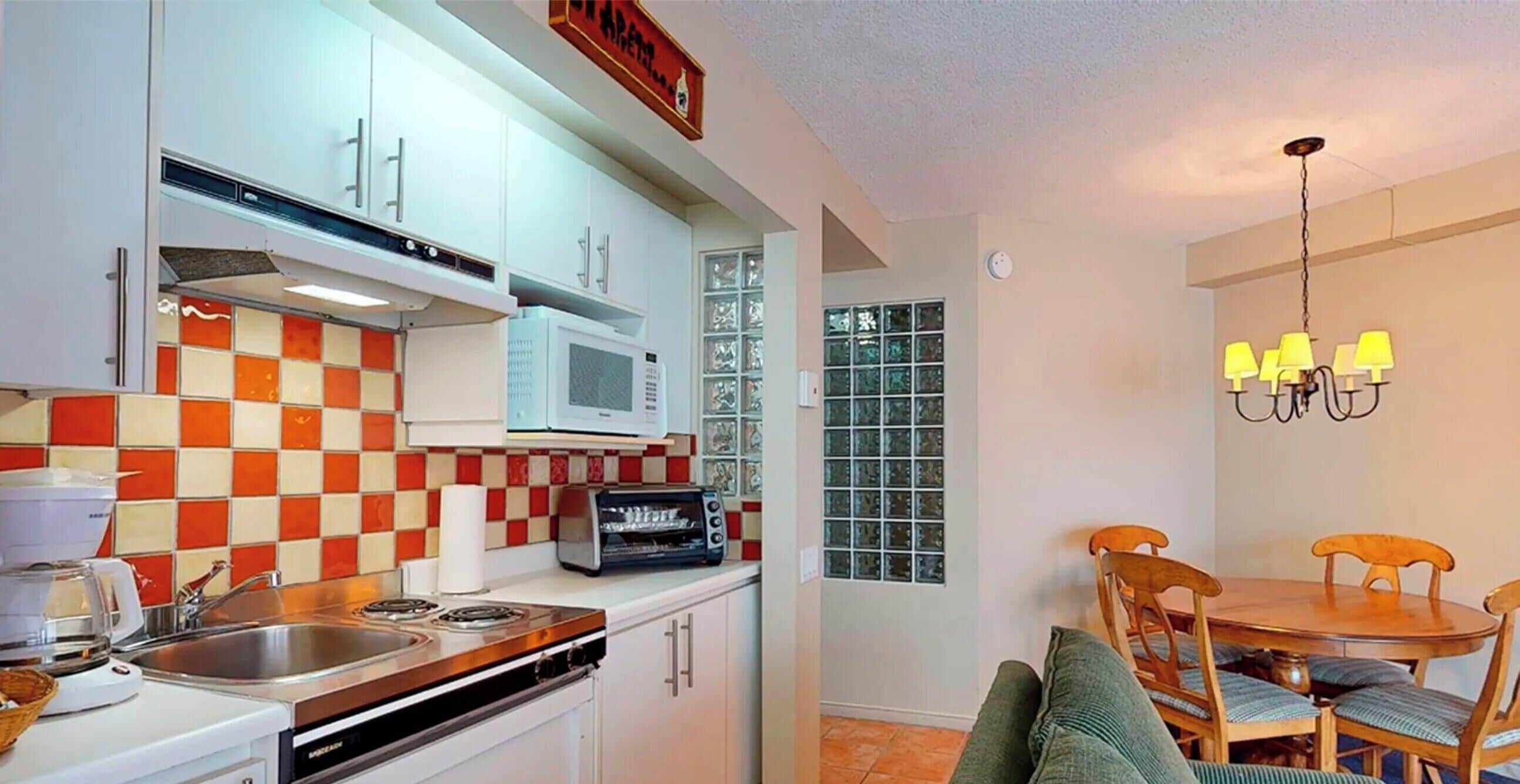 Une cuisine compacte équipée d’un four à micro-ondes, d’un grille-pain et d’une cuisinière, un coin repas avec une table et des chaises, et un lustre.