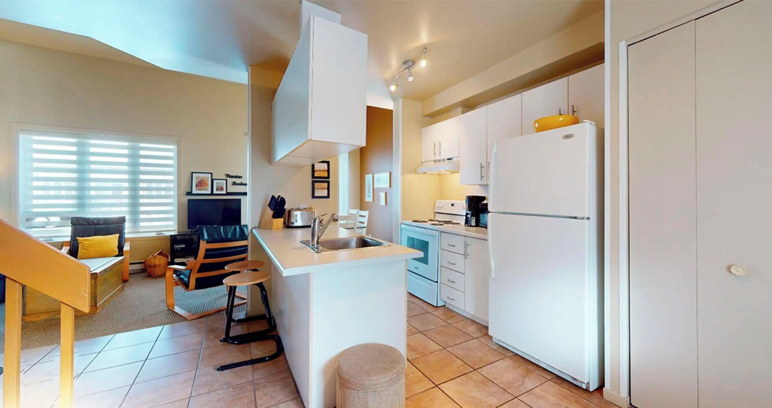 Un espacio habitable compacto con kitchenette, comedor y zona de estar con sofá y sillas.