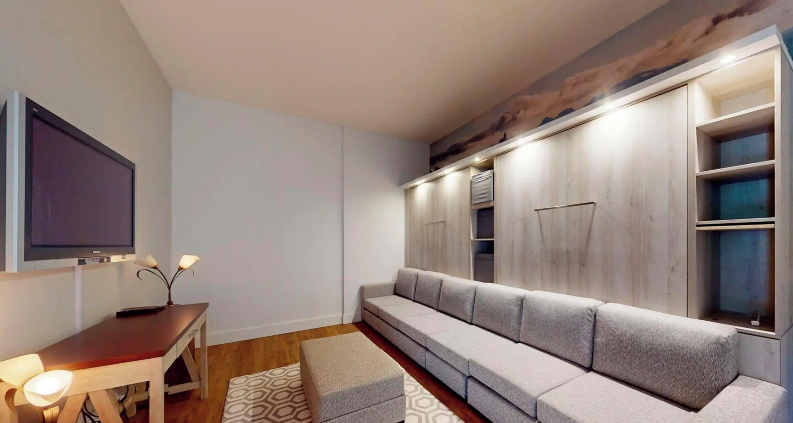 Una sala de estar moderna con un televisor de pantalla plana, una mesa de centro de madera, un sofá gris y armarios empotrados.