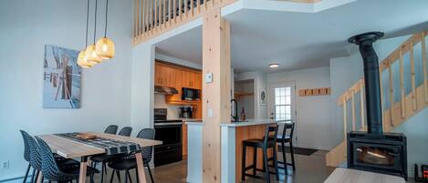 A modern kitchen with wooden cabinets, a dining area with a table and chairs, and a wood-burning stove.