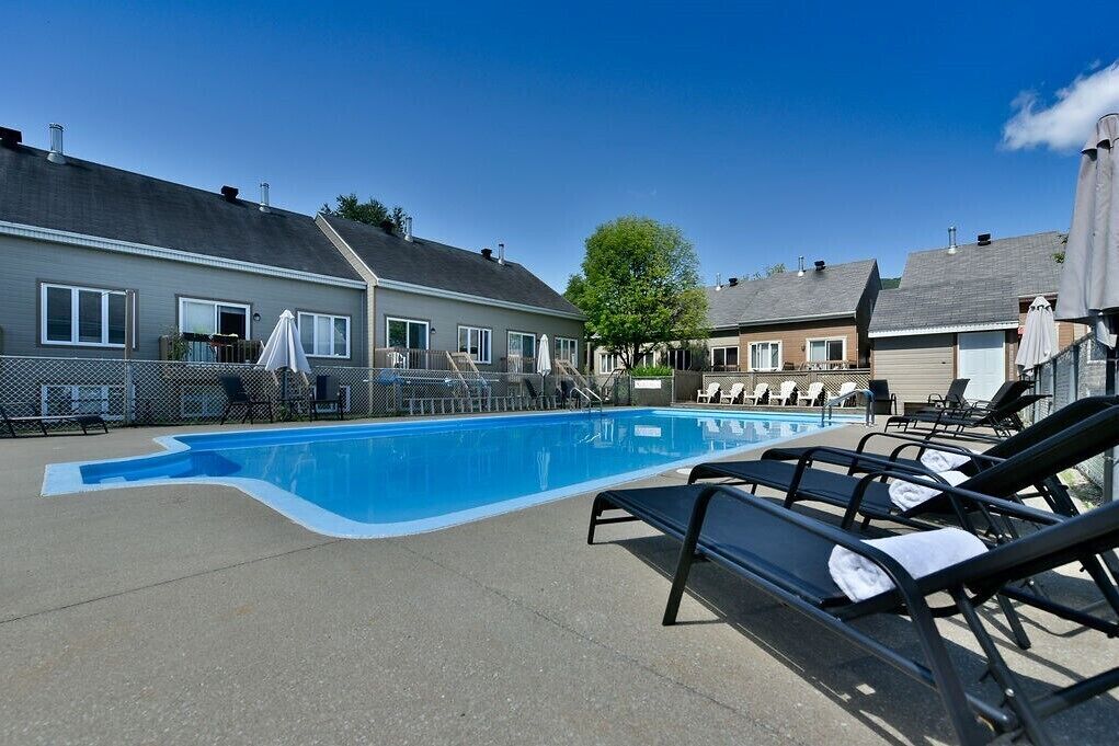 A swimming pool with lounge chairs and a covered area, surrounded by residential buildings.