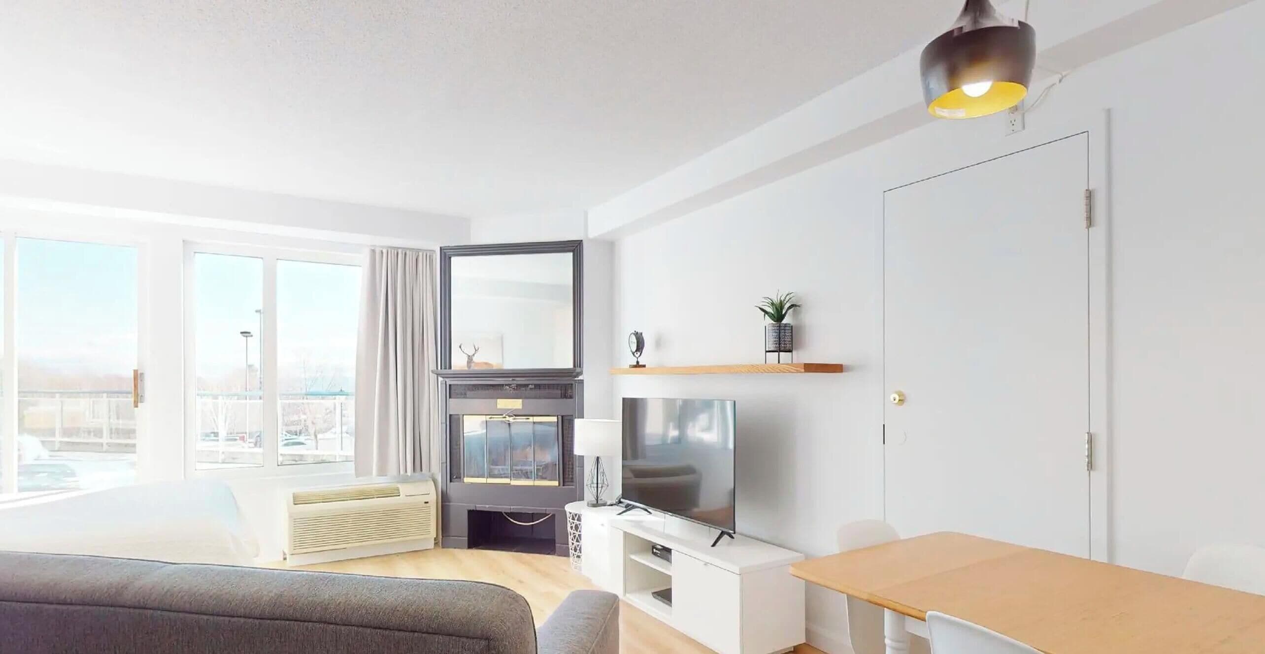 A modern living room with a sofa, a TV, a fireplace, and a large window.