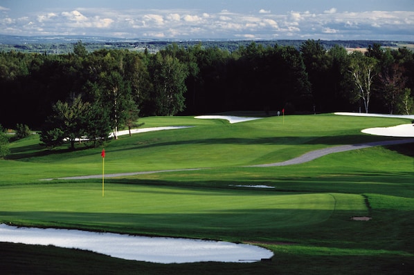 Un parcours de golf avec des bunkers de sable, un mât de drapeau et un ciel dégagé.