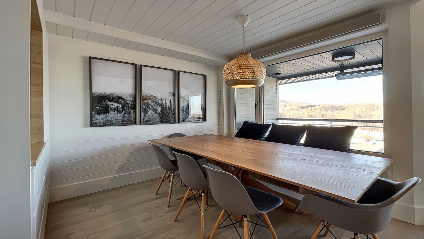 Un comedor con una mesa y sillas de madera, cuadros en la pared y un ventanal con vistas.