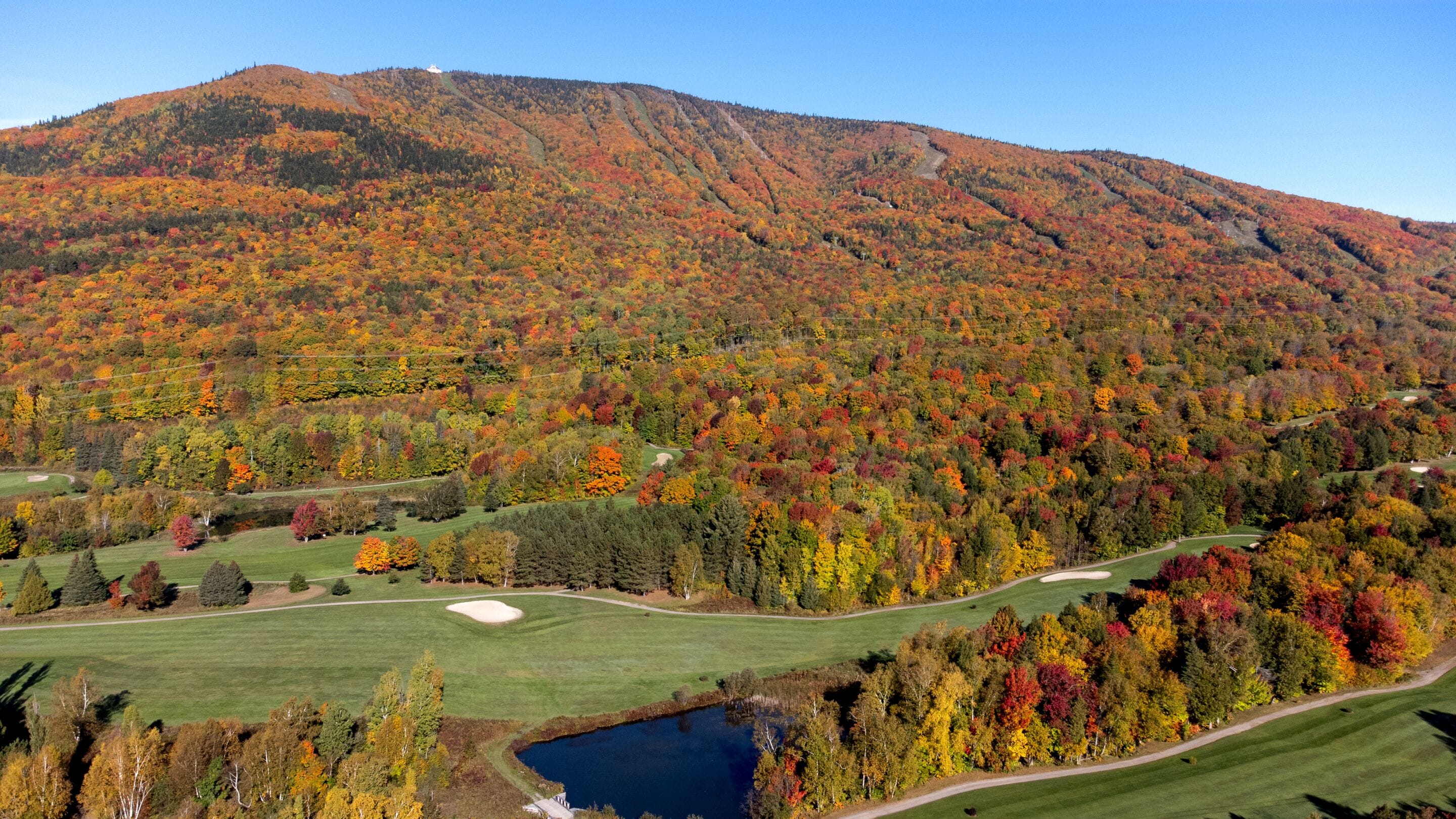 Ein Golfplatz mit einem See, umgeben von Bäumen in Herbstfarben und einem Berg im Hintergrund.