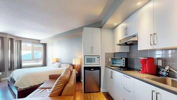A hotel room with a bed, a sofa, a kitchenette, and a window with curtains.
