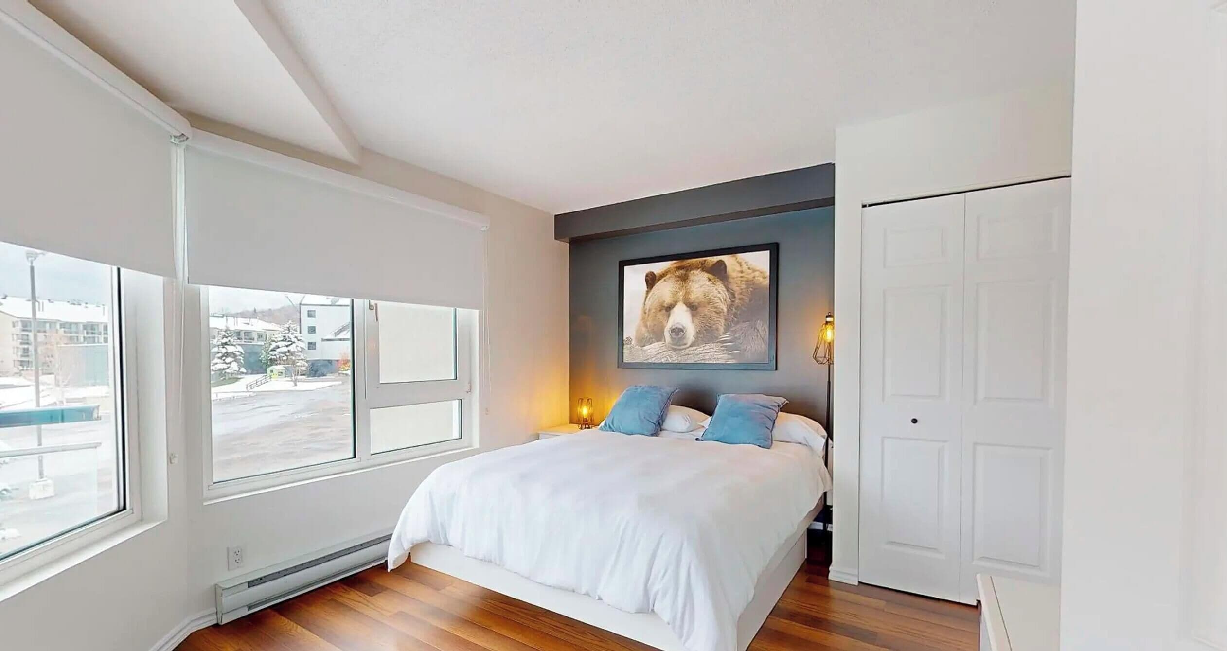 A bedroom with a large bed, a window, a wall-mounted picture, and a door.