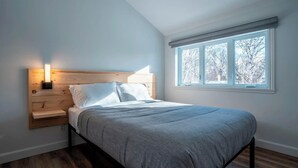 Un dormitorio con cama, mesita de noche y ventana con vistas a árboles.
