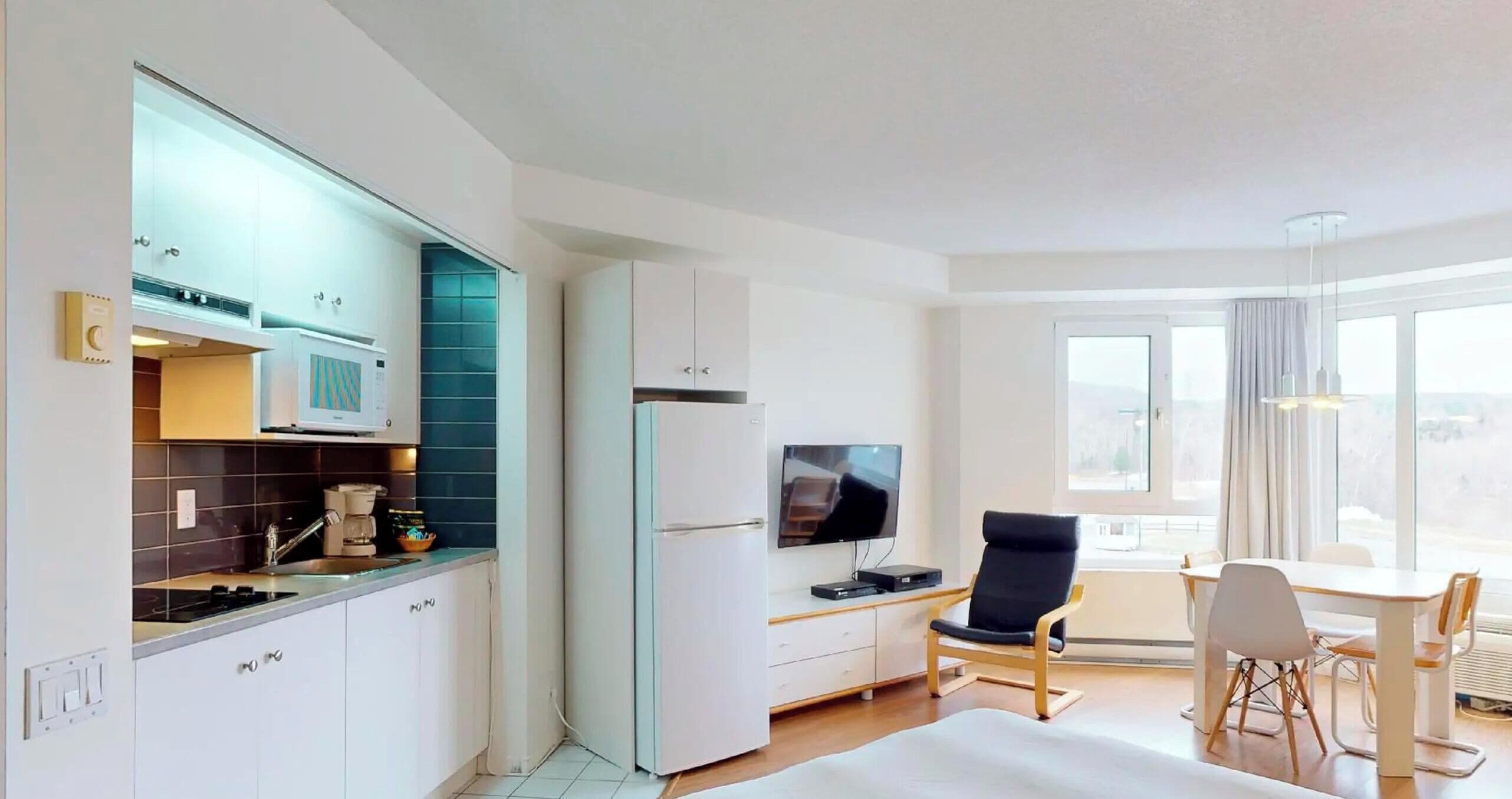 Ein modernes Hotelzimmer mit einer Küchenzeile, einem Essbereich und einem großen Fenster.