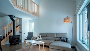 Una sala de estar moderna con una estufa de leña empotrada, un sofá, una mesa de comedor y una escalera.