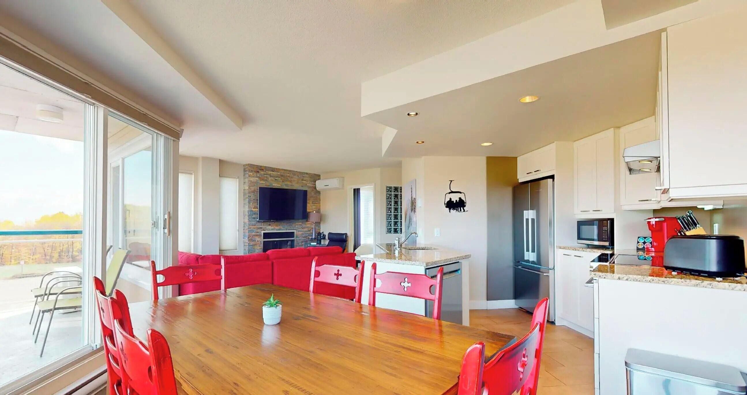 A modern kitchen with a dining area, a TV mounted on the wall, and a view of the outdoors.
