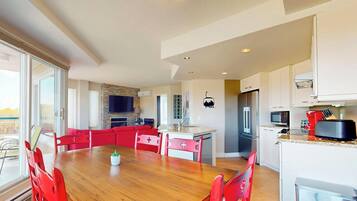 A modern kitchen with a dining area, a TV mounted on the wall, and a view of the outdoors.