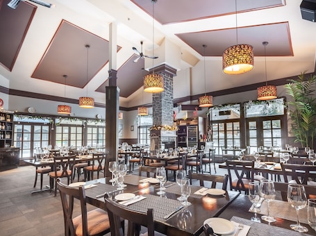 A spacious restaurant with high ceilings, large windows, and multiple dining tables set with wine glasses and plates.
