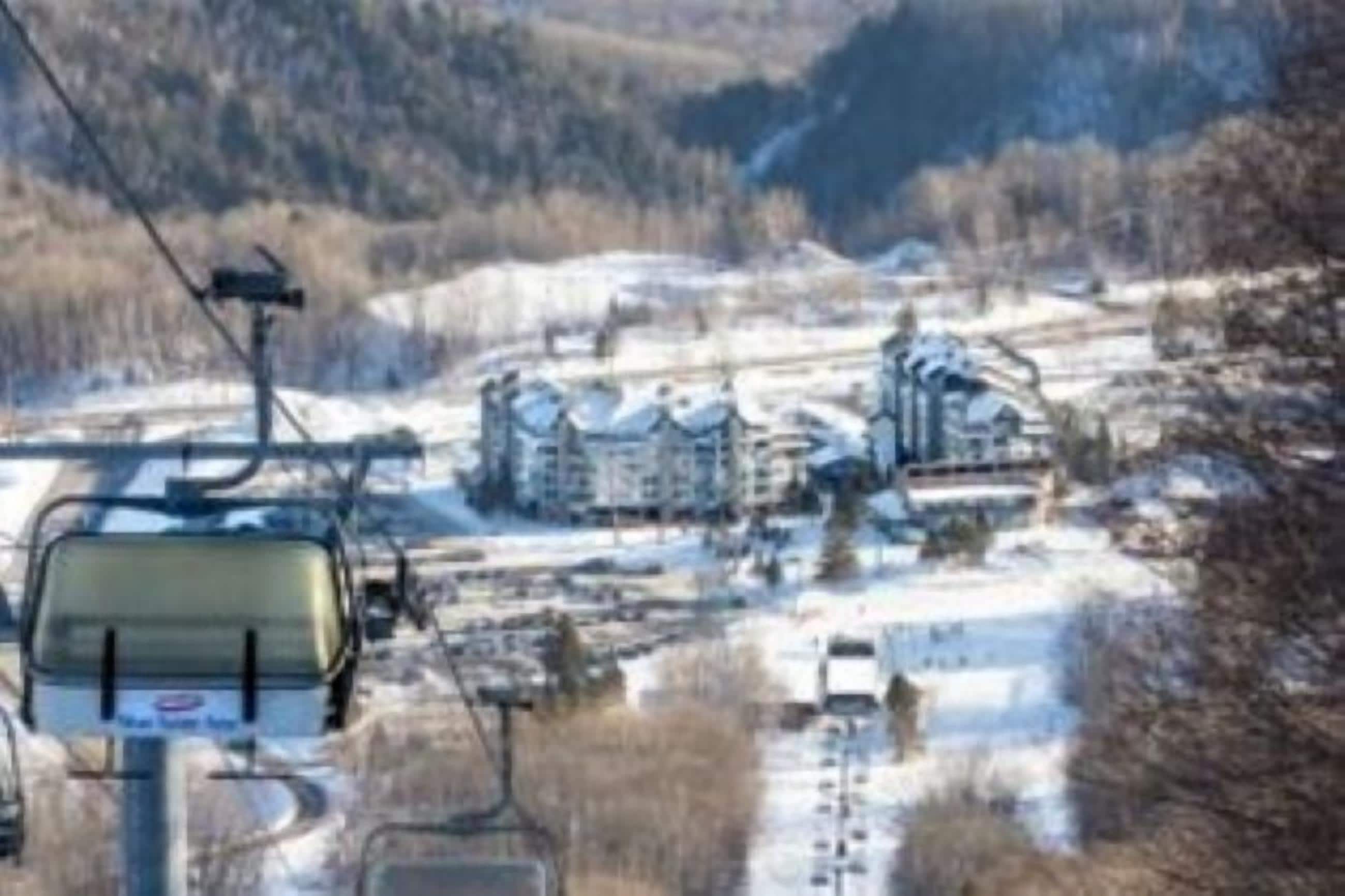 A ski lift with a chairlift and a mountainous landscape with buildings in the background.