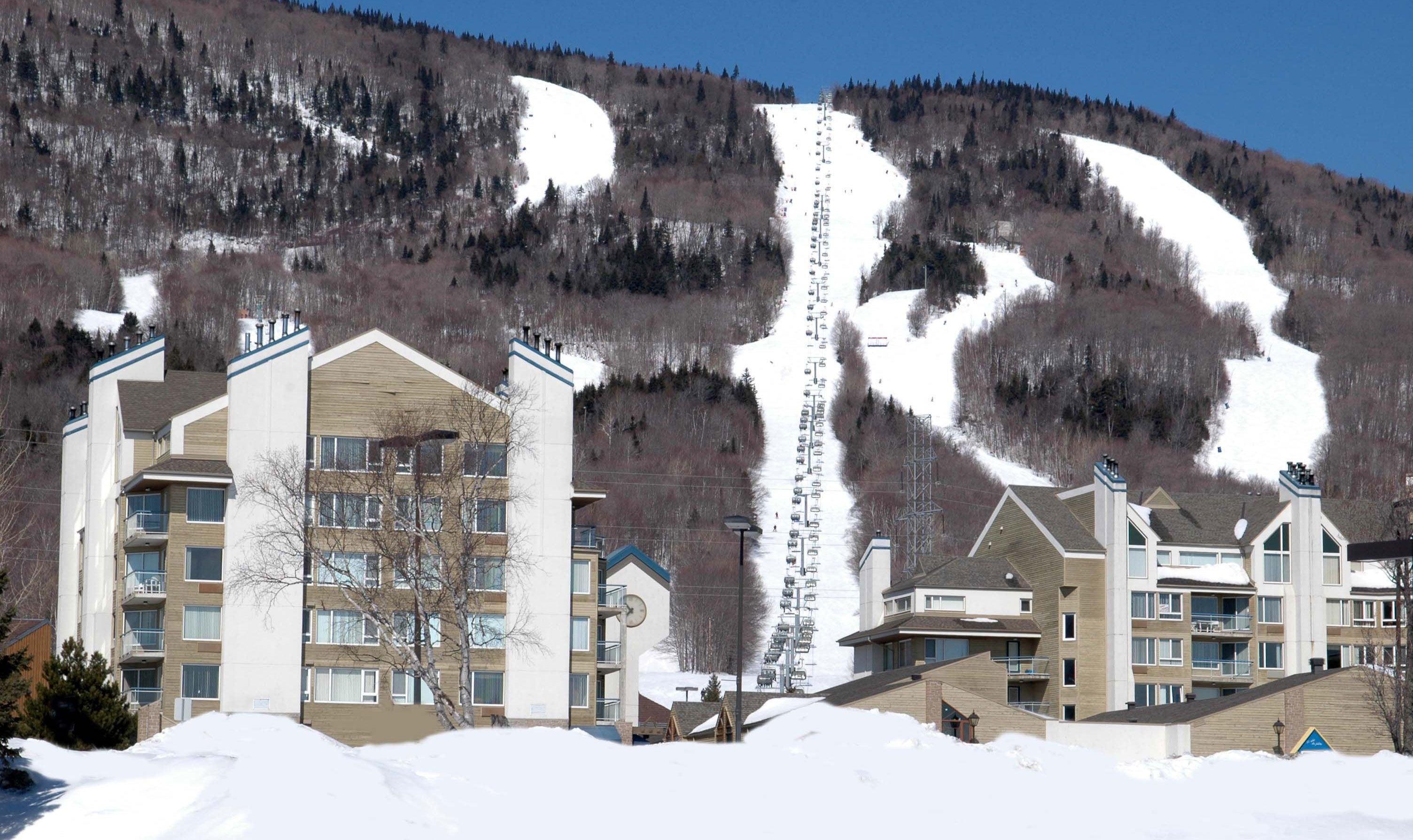 Une station de ski avec des bâtiments à plusieurs étages, un télésiège et un paysage montagneux en toile de fond.