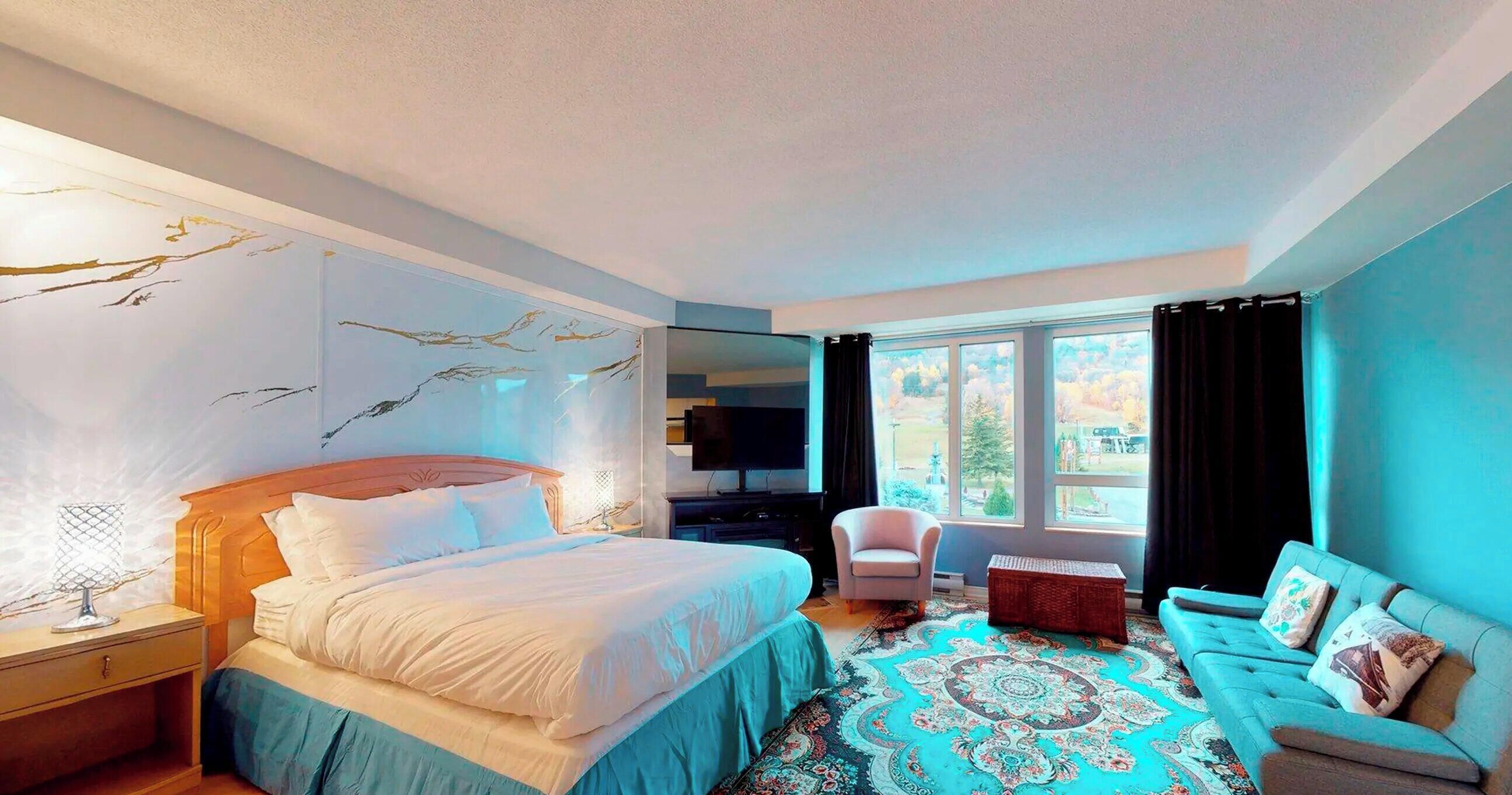 Une chambre d’hôtel avec un lit, une télévision, une chaise, un canapé et une grande fenêtre avec des rideaux.