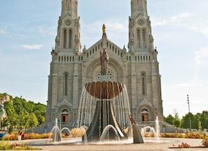 A large cathedral with twin towers and a central statue. In front, there is a fountain with water jets and a sculpture.