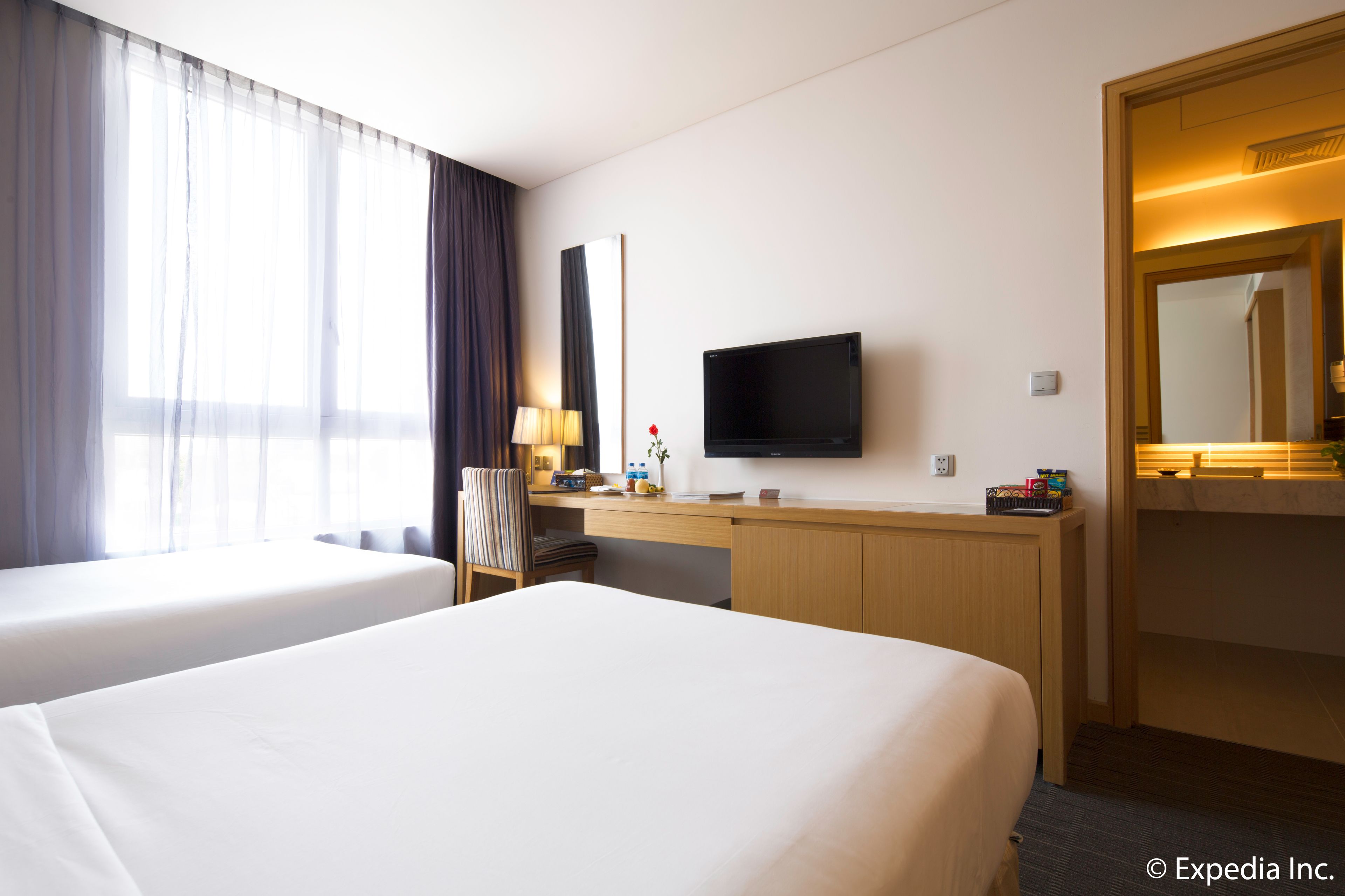 A hotel room with two beds, a desk with a flat-screen TV, a mirror, and a window with curtains.