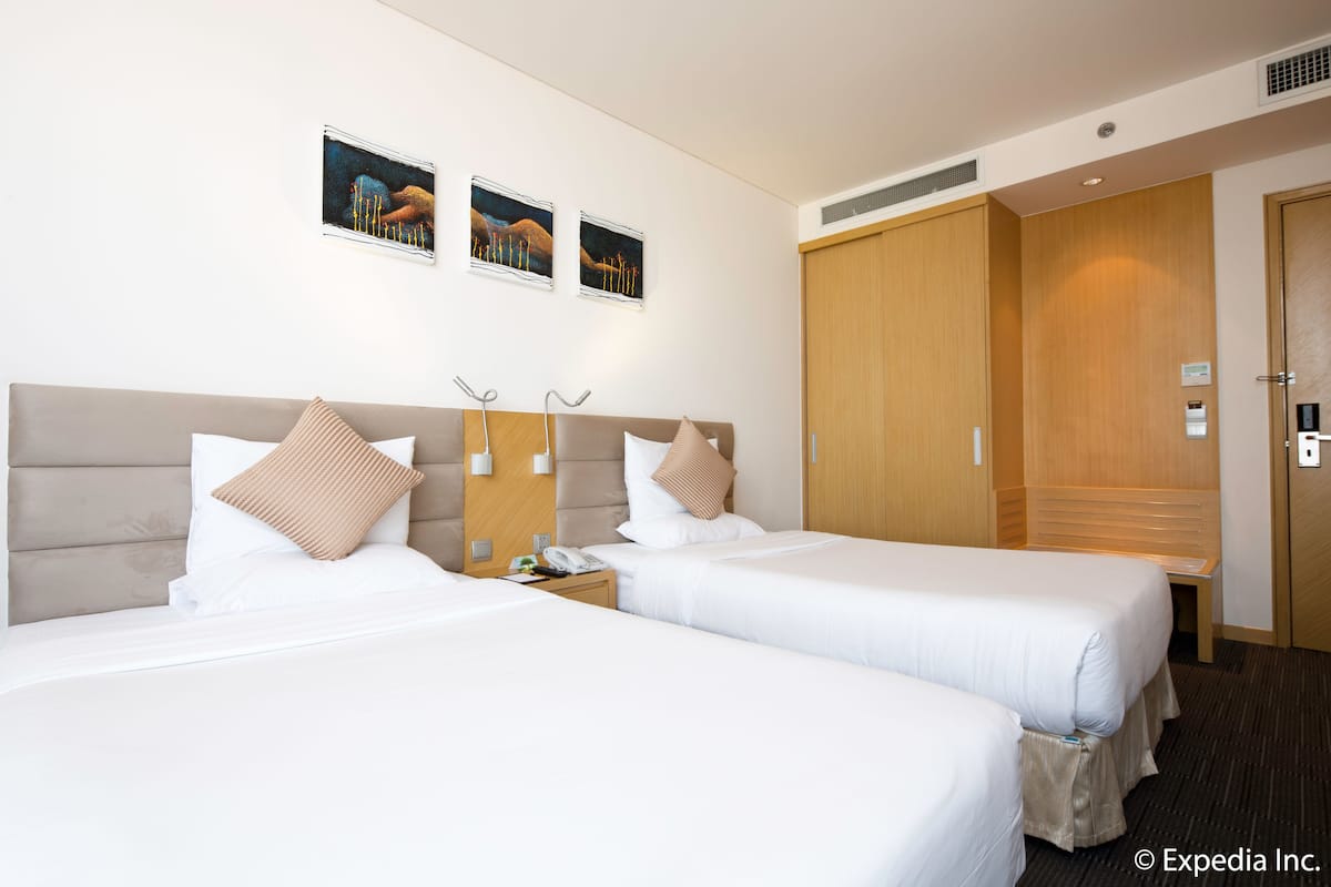A hotel room with two beds, a wooden wardrobe, a nightstand with a phone, and wall-mounted artwork.
