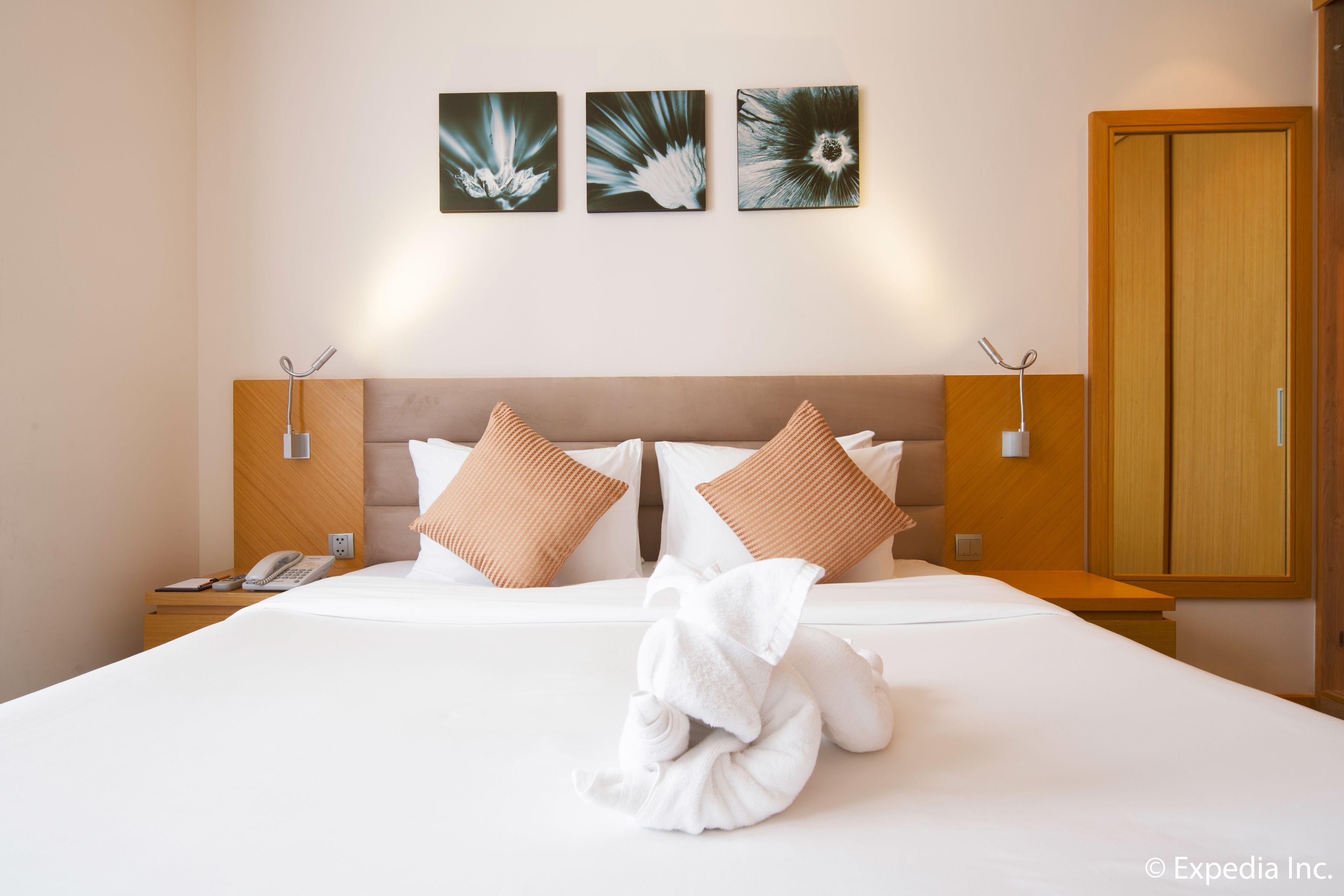 Ein Hotelzimmer mit einem großen Bett, zwei Wandleuchten, einem Holzschrank und drei gerahmten Kunstwerken an der Wand.